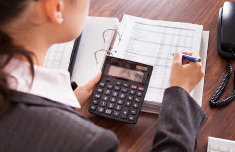 Woman calculating finances Over shoulder view of businesswoman calculating finances in office